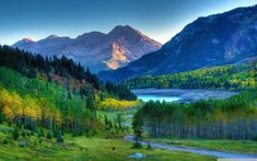 the mountains are covered in trees and green grass, with a river running between them