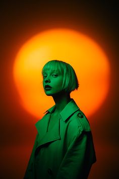 a woman with green hair in front of an orange background and the sun behind her