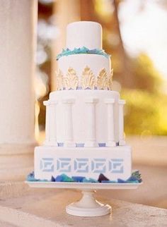 a white and blue wedding cake sitting on top of a table next to a pillar