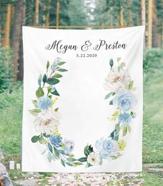 a wedding banner with blue flowers and greenery is displayed in front of a forest