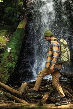 a man with a backpack walking in front of a waterfall