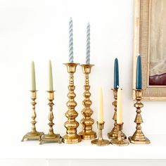 candles are lined up on a mantle in front of a painting and an old portrait