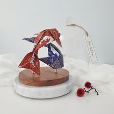 an origami bird on a wooden base next to a red and white flower