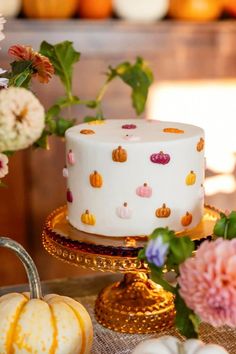 a white cake sitting on top of a wooden table next to flowers and pumpkins