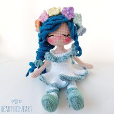 a crocheted doll with blue hair and flowers on her head, sitting in front of a white background