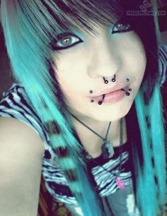 a girl with blue hair and piercings on her face is posing for the camera