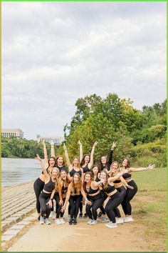 a group of young women standing next to each other in front of a lake and trees