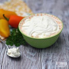 a green bowl filled with whipped cream next to peppers and carrots on a wooden table