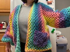 a woman standing in front of a refrigerator wearing a multicolored crocheted sweater