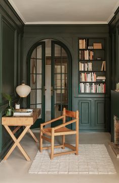 a chair and table in front of a green door with bookshelves on either side