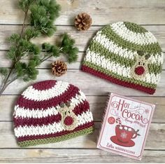 two crocheted hats sitting on top of a wooden table next to pine cones