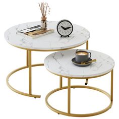 two white marble tables with gold legs and a clock on the top one table has a black coffee cup in front of it