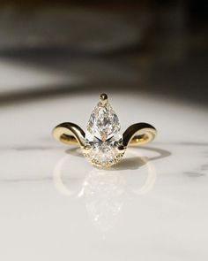 a yellow gold ring with a pear shaped diamond in the center on a white surface