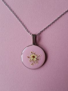 a pink necklace with a flower on the front and back of it, hanging from a silver chain