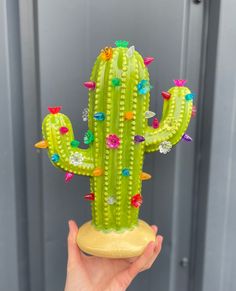 a hand holding a green cactus with lots of colorful spikes on it's head