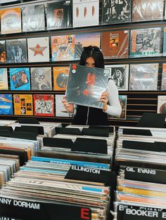 a woman holding up a vinyl album in front of a wall full of records and cds