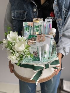 a woman holding a basket with flowers and personal care items in it, all wrapped up