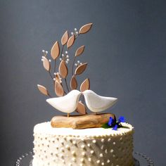 two white birds on top of a cake decorated with leaves and flowers, one is kissing the other