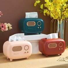 three different colored radio speakers sitting next to each other on a table with flowers in the background