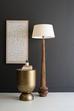 a lamp sitting next to a gold vase on top of a white floor near a painting