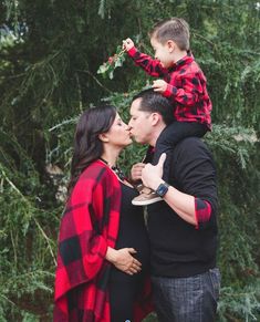 a man and woman kiss their son as they stand in front of some trees while the child stands on top of them