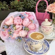 a bouquet of pink flowers sitting on top of a table next to a cup of coffee