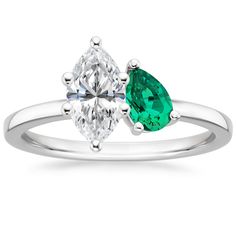 an engagement ring with two pear shaped emeralds on the side and a diamond in the middle