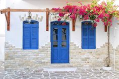 blue doors and windows on a white building with pink flowers growing out of the windows