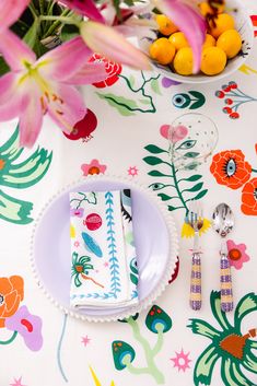 a table topped with plates and bowls filled with fruit next to flowers on top of a white table cloth