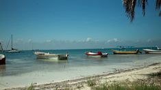 several boats are docked on the beach near the water's edge, while another boat is in the distance