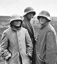 three men in trench coats and helmets standing next to each other on a grassy field