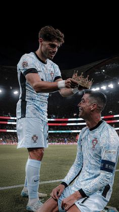 two soccer players are sitting on the field and one is holding a crown while the other looks at him