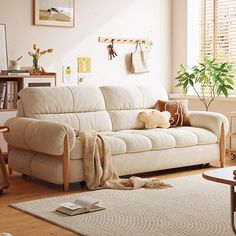 a living room with a white couch and wooden table next to a window filled with plants