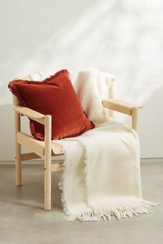 a wooden chair with a red pillow on top of it and a white blanket over the back