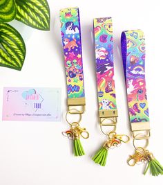 three colorful lanyards with tassels attached to them and a plant in the background