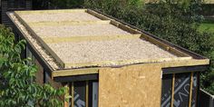 a building that is being built with wood and gravel on the roof, surrounded by trees