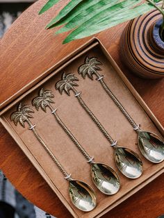 four spoons with palm trees on them are sitting in a box next to a potted plant