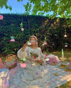 a woman is sitting on a picnic blanket with flowers in her hair and holding a phone up to her ear