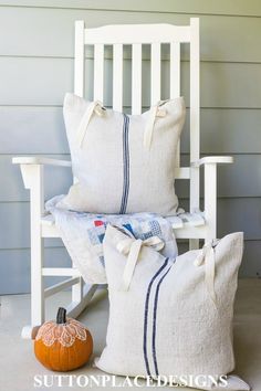 two pillows sitting on top of a white rocking chair next to a pumpkin and pillow