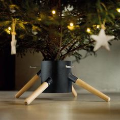 a small christmas tree in a black pot with wooden legs and two white stars on the top