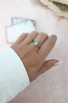 a woman's hand wearing a gold ring with a turquoise stone in the middle