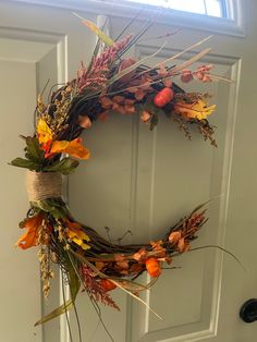 a wreath is hanging on the front door with dried flowers and leaves around it,