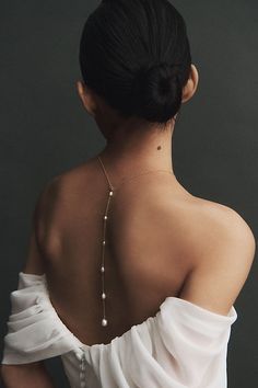 a woman wearing a white dress with pearls on her neck and shoulder, back to the camera