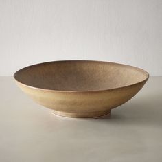 a large brown bowl sitting on top of a table next to a white wall and floor