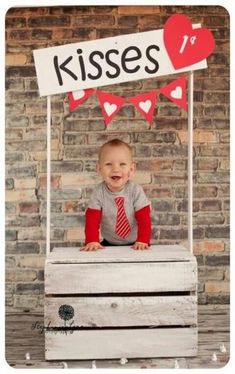 a baby is sitting on top of a wooden crate with a sign that says kisses