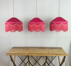 three pink lamps hanging over a wooden table