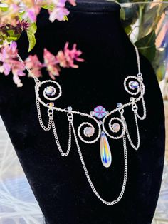 This swirly chandelier necklace has a beautiful rainbow Quartz doublet briolette bead and a Czech glass flower bead at its focal point 🌼🌈✨ round 18 gauge sterling silver wire is designed in an elegant S shape, swirling at each end with accent beads attached. Smaller round 26 gauge wire is coiled around the 18 gauge wire to add to the design. The smaller wire also creates more depth to the piece and is used to weave smaller accent beads onto it. Silver chain drapes off the wire to give it a chandelier appearance. The necklace sits nicely on the neckline, measuring 14 inches, with a lobster clasp closure. Chandelier Necklace, Tempe Az, Rainbow Quartz, Wire Necklace, Crystal Choker, Necklace Crystal, Beautiful Rainbow, Quartz Necklace, Beaded Flowers