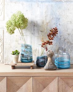 three vases with flowers in them sitting on a wooden table next to a wall