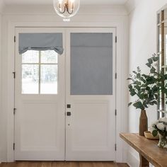 a white front door with two windows and some flowers on the side table next to it