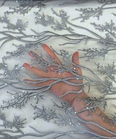 a woman's hand is covered with silver beads and sequins on a white fabric